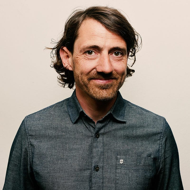 Porträt von Nico Brückner, Inhaber der knallorange® GmbH, in grauem Hemd vor neutralem Hintergrund